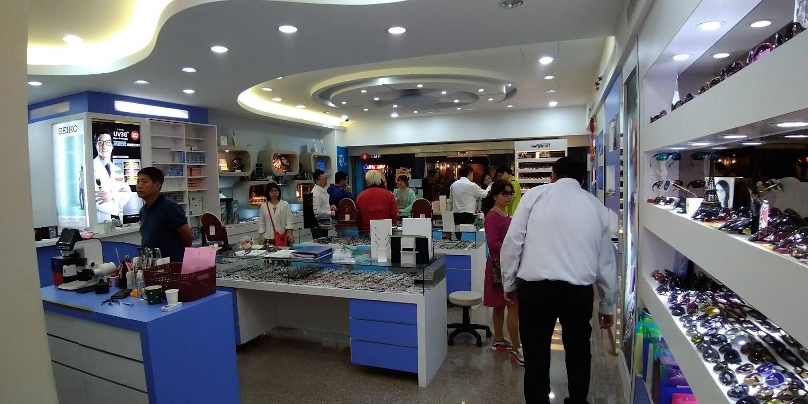 三峽眼鏡行內部，門口透過玻璃窗有熟客對驗光師揮手，店內氣氛溫馨熱絡